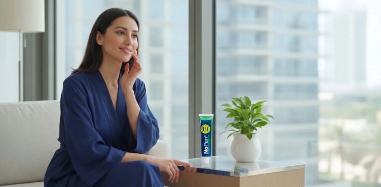 Woman in a blue robe relaxing next to NoPain numbing cream with a city skyline view.